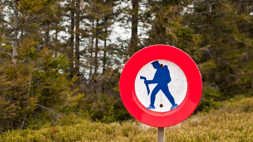 A forest scene featuring a red circle hiking prohibition sign indicating restricted access.
