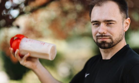 Adult man holding a protein shake outdoors during the day.